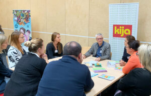 Teilnehmer:innen sitzen beim Stationentisch der Kiknder- und Jugendanwaltschaft Burgenland und tauschen sich aus.