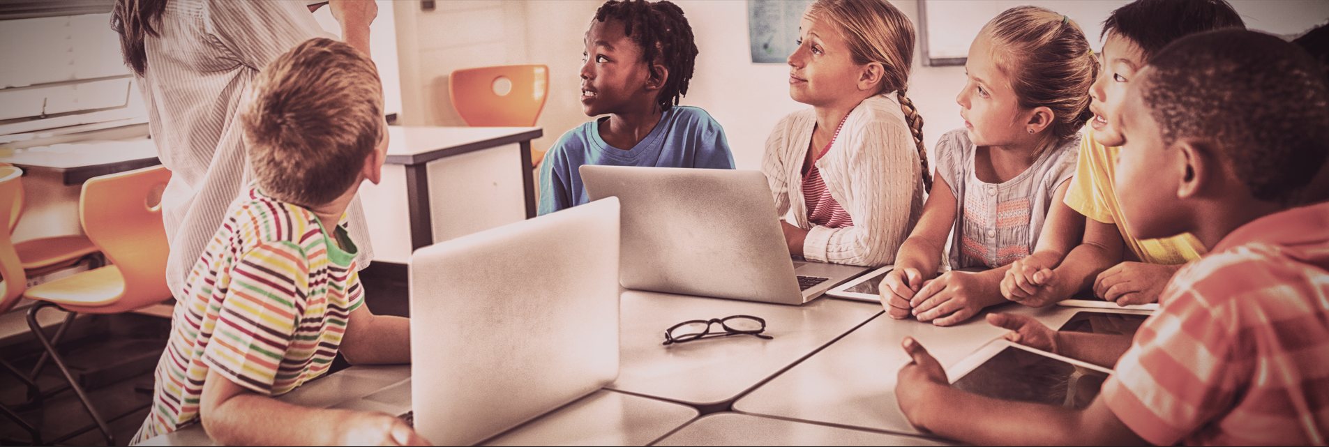 Lehrerin zeigt Schülerinnen am Computer neue Medien.